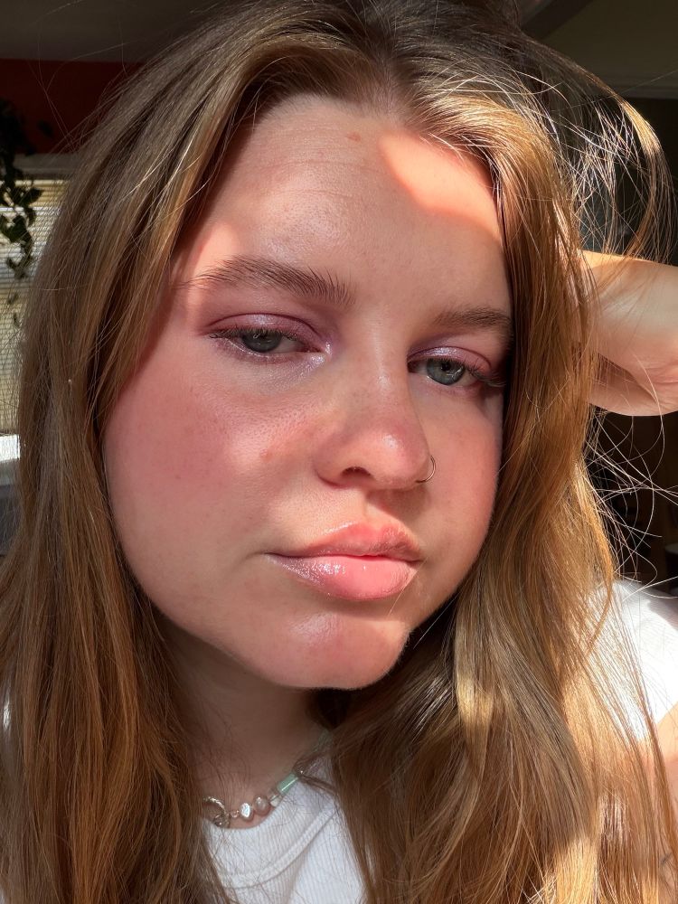 a selfie of jori. she has long light brown hair and is resting a hand on her head and she has purple sparkly makeup on