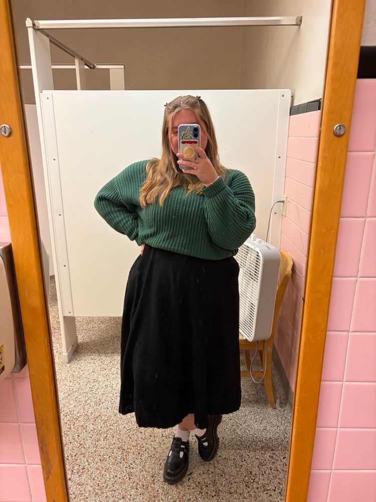 a mirror selfie of jori, she is wearing a black maxi dress with a green sweater over it and black Mary Jane’s with white socks