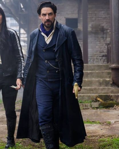 The character Vikram from The Librarians: The Next Chapter. He is a dark haired man with a goatee, dressed for the mid to late 1800s. He is wearing a calf-length overcoat, a double-breasted waistcoat with a watch chain, and an ascot.