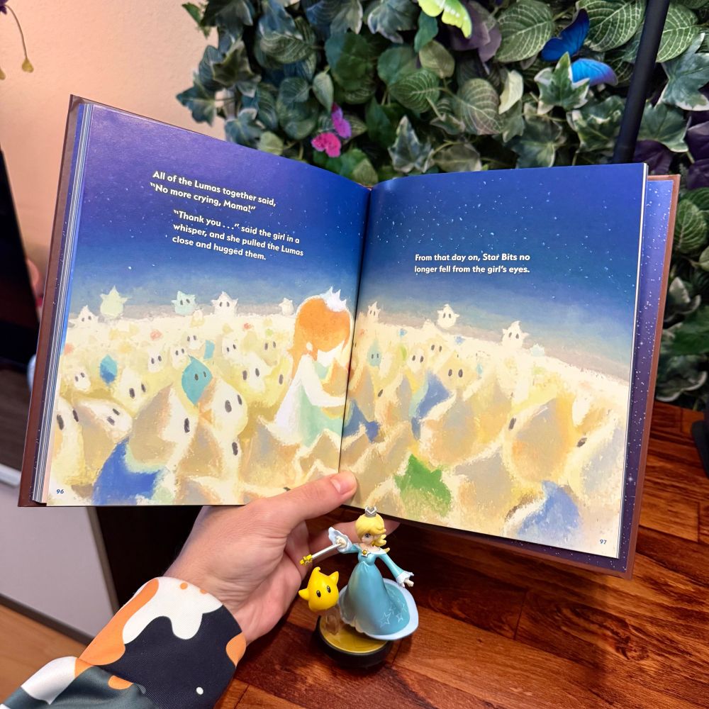 Foto del libro por una de sus páginas en las que aparece Estela de niña rodeada de un montón de Destellos. Junto al libro hay un amiibo de Estela y Destello de Smash Bros.