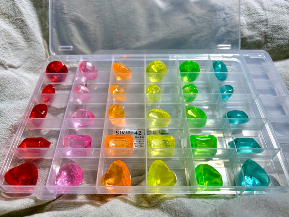 宝石型の透明プラスチックを色・形状別に仕切り付きの箱に並べたところ