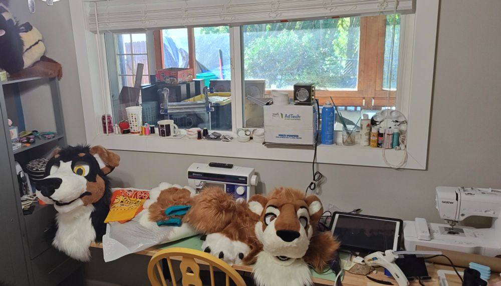 A cluttered workshop with several fursuit heads and a lot of sewing machines.