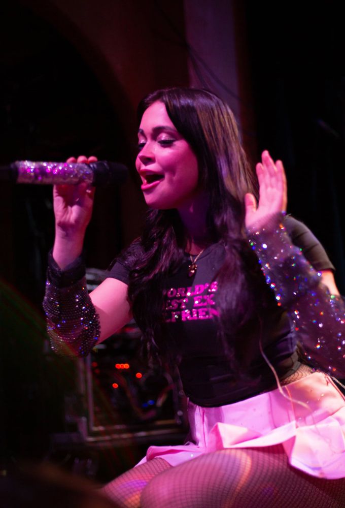 The same woman as the first image. She’s on her knees singing into the mic. 