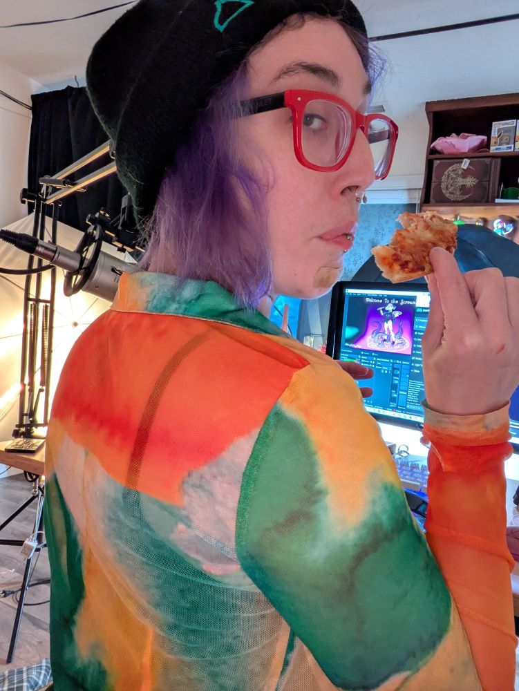 Viridian is now turned, looking back over their shoulder toward us (the camera). They are looking very nonchalant while munching on a slice of cheese pizza. 