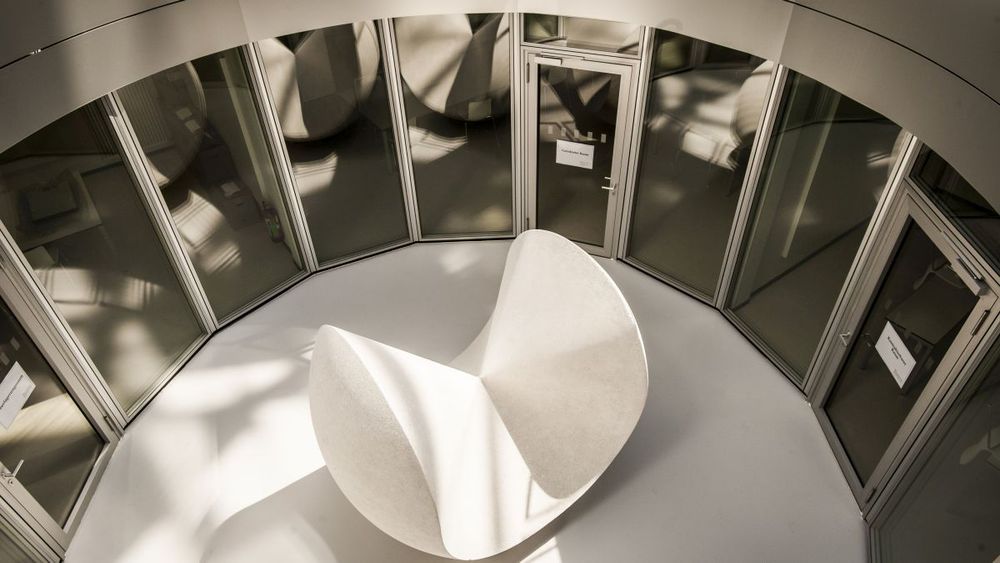 Eine abstrakte weiße Skulptur inmitten eines kreisrunden, von einer Glasfassade eingefassten Innenhofs.