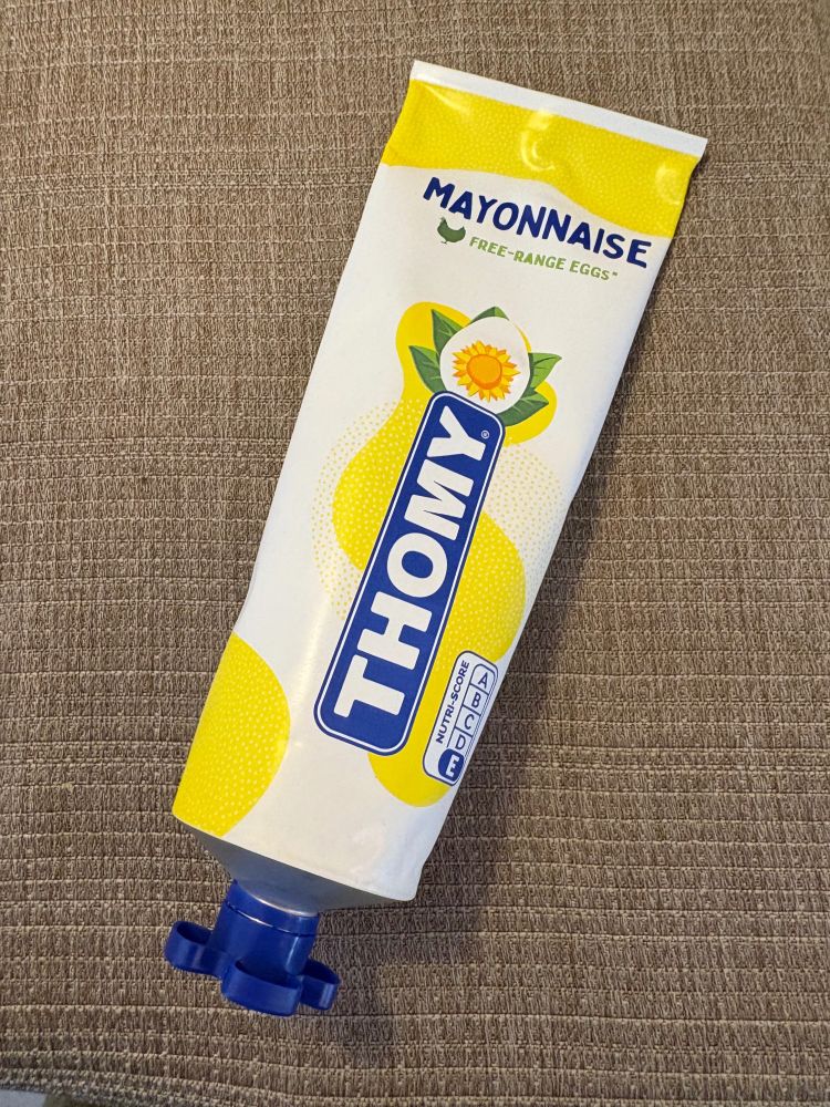 A tube of Thomy brand mayonnaise on a brown tablecloth. 