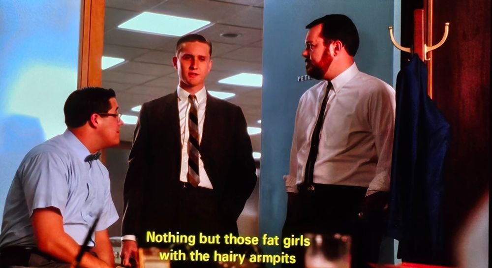 foto de uma cena de mad men. 3 homens brancos com camisa de botão em um escritório. a legenda diz "nothing but thoss fat girls with the hairy armpits"