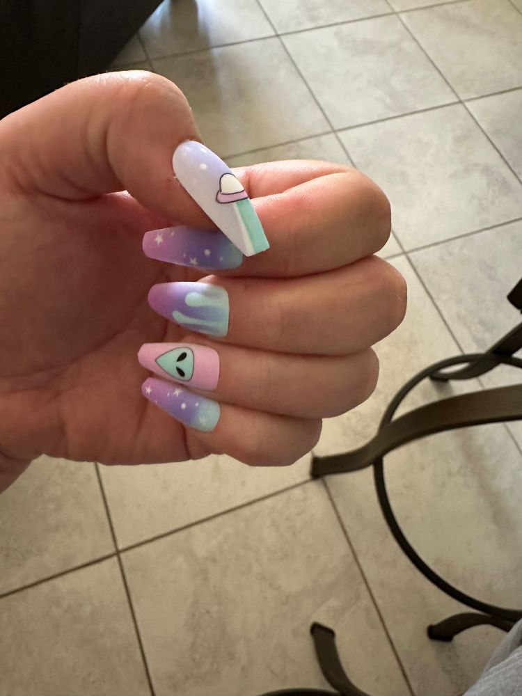 A photo of my hand looking like I’m giving an invisible handjob (because A: it’s hilarious, and B: there’s so few ways to photograph your own nails). The nails are decorated with illustrated press on long coffin nails in pastel aqua, pink, and lavender. The designs from top-bottom: a flying saucer beaming up, starry twilight, slimy drips down an ombré background, an alien face on a pink background, and another starry twilight