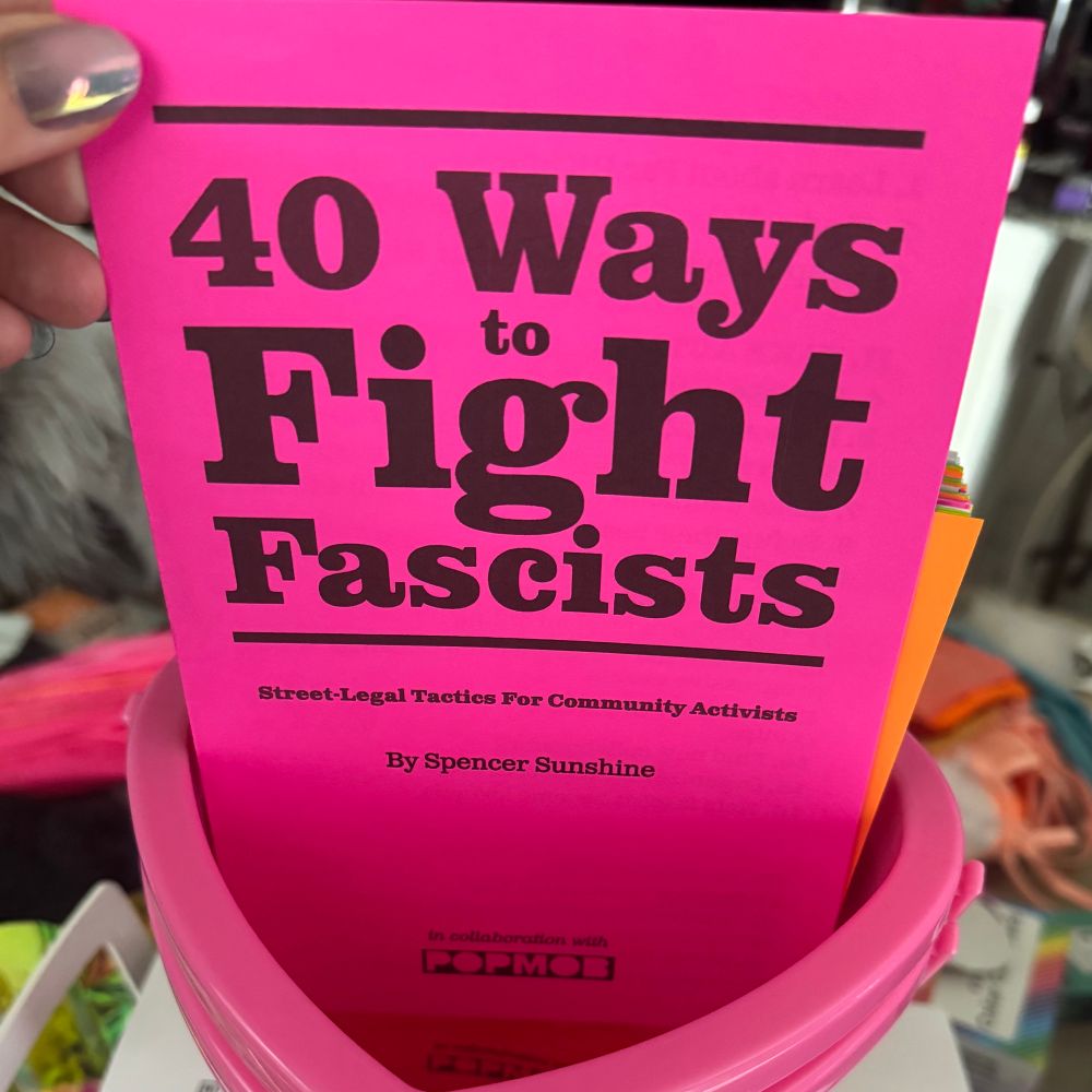 A photo of a pink heart-shaped candy bucket with a pink pamphlet zine titled “40 Ways to Fight Fascism” by Spencer Sunshine.