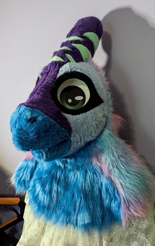 An image of a fursuit head taken at an angle. The fursuit head is made of purple, blue, and mint colored fur
