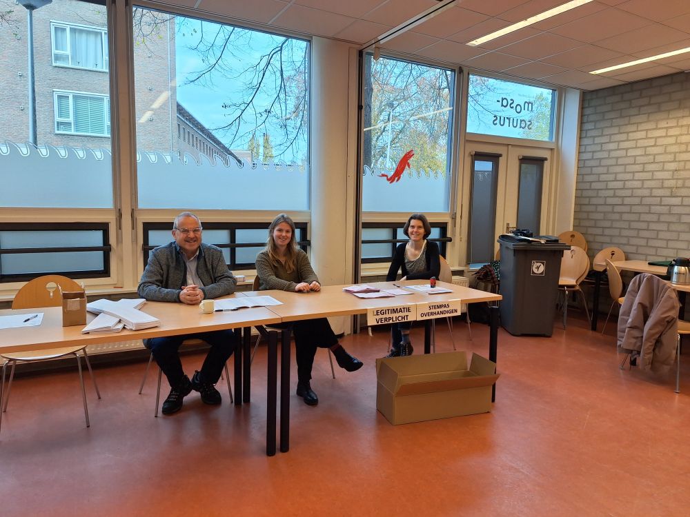 Drie stembureauleden op een rijtje achter de tafels.