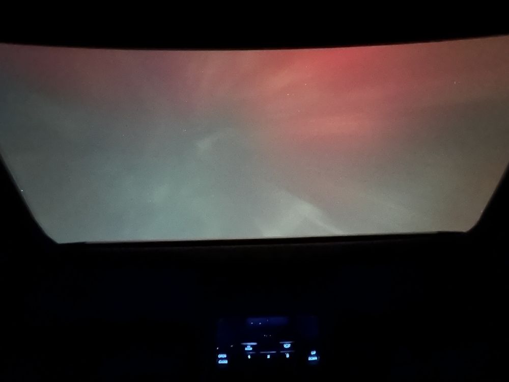 Intense red and green aurora seen framed by dark outline of a car sunroof opening.
