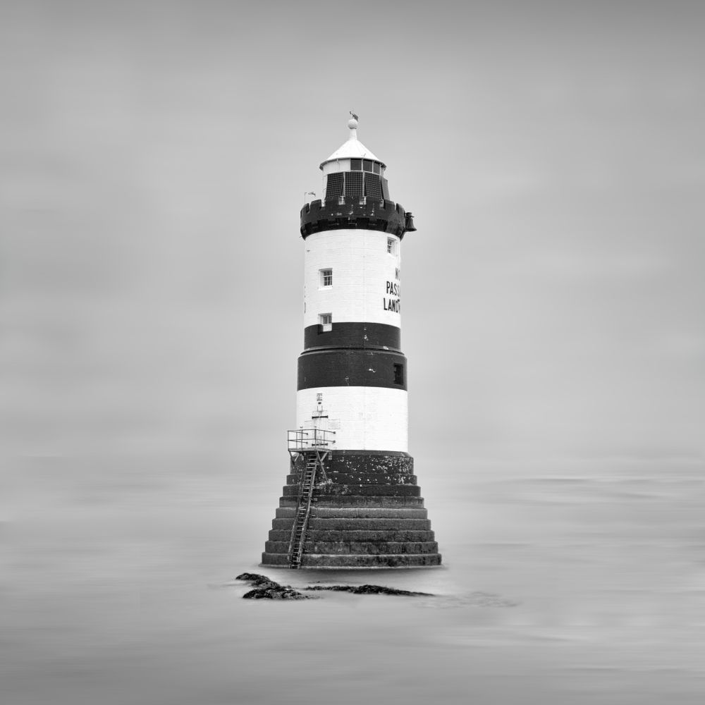 A minimalist long exposure of Penmon lighthouse in Wales.  The shot was taken at high tide on a very grey day and is presented as a square crop in black and white.  The scene is limited to the foreground sea, a couple of rocks and the lighthouse centrally placed.  The horizon has been blended with the sky to further simplify the scene.
