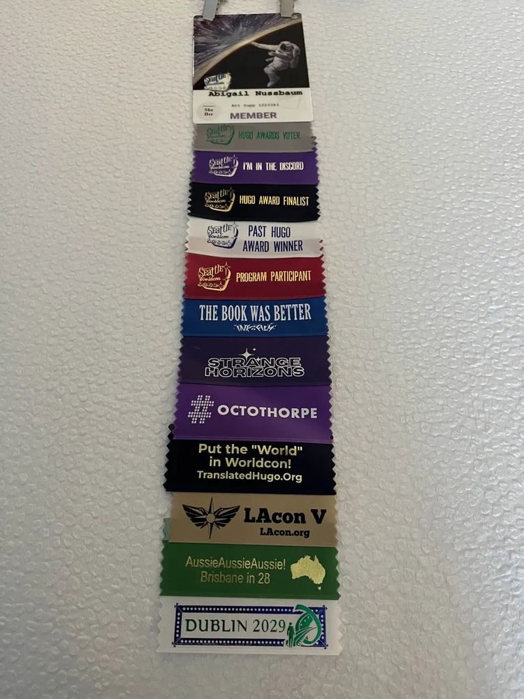 A Worldcon 2025 membership badge with many attached ribbons