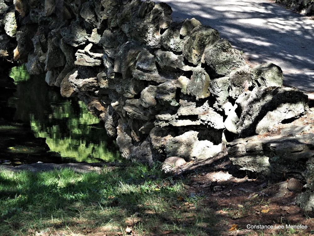 Portion of stone foot bridge with water showing that is green with reflections of trees - dappled light