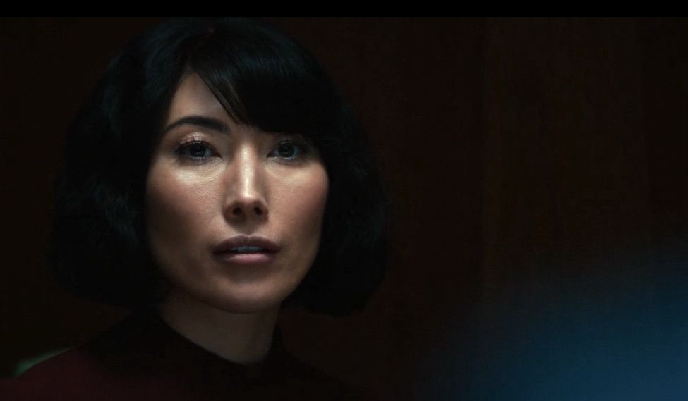 A screenshot of Ms Casey from Severence, a woman looking direct but emptily at someone else out of sight. 