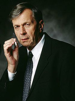 William B. Davis in a promotional photo as the Cigarette Smoking Man from the television series The X-Files. This character was also referred to as the "cancer man." He's wearing a suit and scowling with his entire face while holding a lit cigarette in his right hand near his mouth.