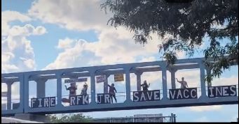 People on overpass with letters spelling: Fire RFK Jr Save Vaccines 