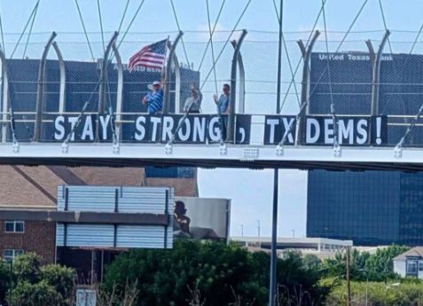 People on an overpass holding letters that spell: Stay strong TX Dems
