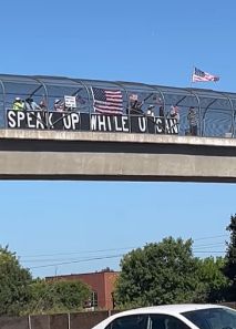People on an overpass with letters spelling: Speak Up While U Can