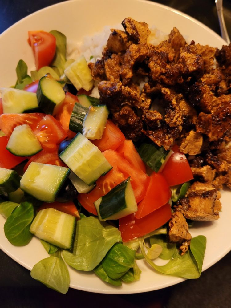 Valkoisella lautasella vihersalaattia, uunitofua ja riisiä. 