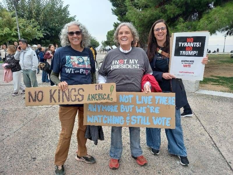 Three people with signs read No kings in America, We may not live there but we’re watching and we vote, No Tyrants, No Trump!
