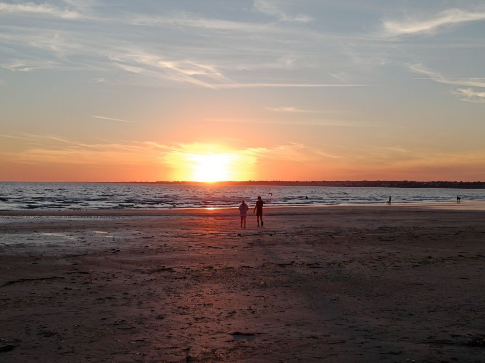 Sonnenuntergang mit zwei Personen, die am Meer stehen.