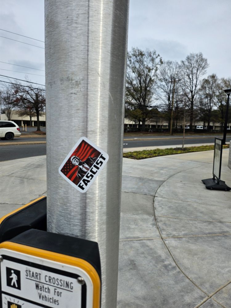 Cross walk pole in Charlotte with a sticker showing Trump, with the word "fascist" below