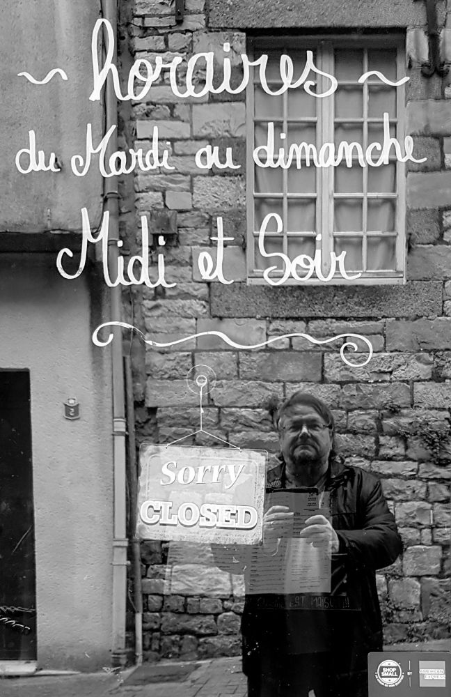 Man takes a phone photograph in a shop window, with the words  - Horaires - du mardi au dimanche Midi et Soir