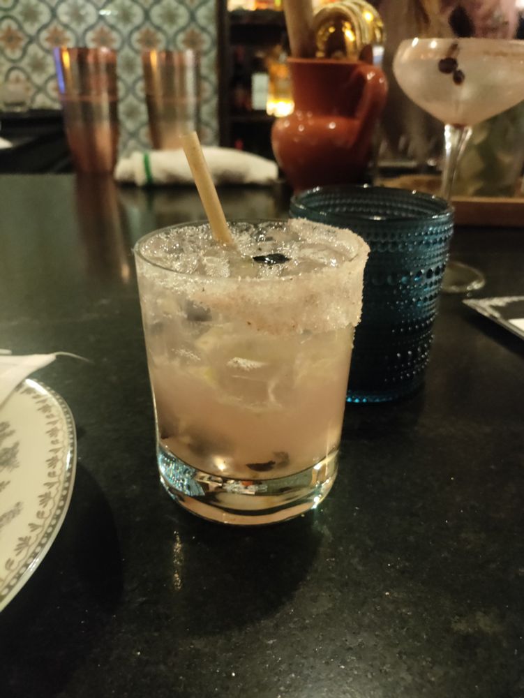 A margarita sits in front of a blue glass of water at a bar. 