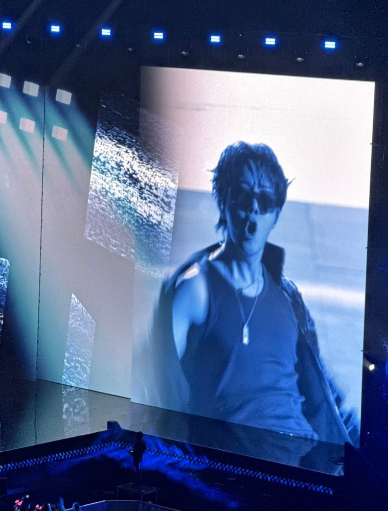 j-hope of BTS on stage in Paris at the Pieces Jaunes charity gala. His shirt has fallen off his shoulder revealing a sleeveless T and his very lovely shoulder and throat. He's singing hard, too.
