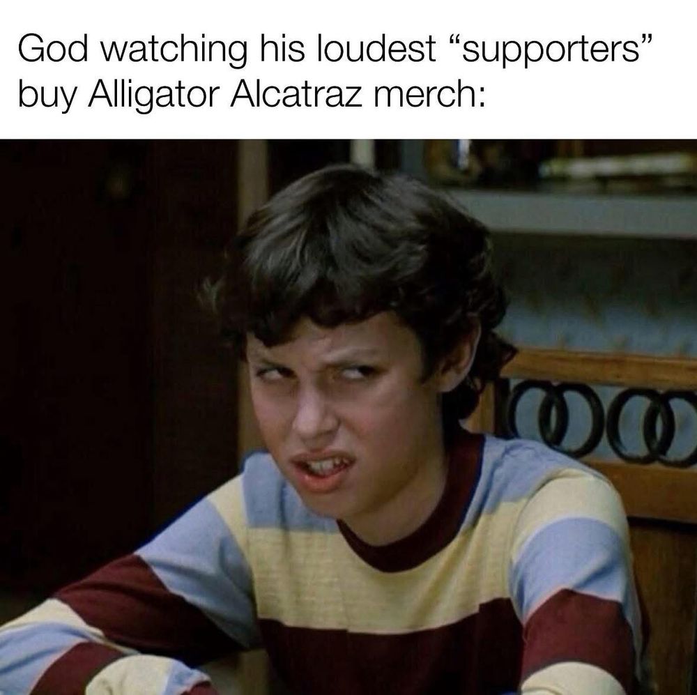 The image is a meme featuring a scene from a TV show where a young person is making a skeptical or disgusted facial expression. The text above reads: "God watching his loudest 'supporters' buy Alligator Alcatraz merch:" The expression of the person in the image humorously conveys disbelief or disapproval, which complements the sarcastic tone of the caption. The character is wearing a striped long-sleeve shirt, and the setting appears to be indoors.