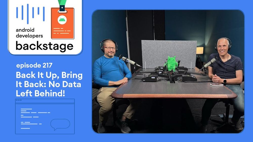 Cover art for "Android Developers Backstage episode 217: Back It Up, Bring It Back: No Data Left Behind!". The left side displays the podcast title with a stylized microphone icon and an orange ID badge featuring the Android robot. The right side shows two individuals in a podcast studio: one with short dark hair, a beard, and glasses, wearing a blue long-sleeved shirt and smiling; the other with short light hair, smiling broadly in a dark short-sleeved shirt. Both are wearing headphones and seated at a dark wooden table with microphones and a green robot plush between them.