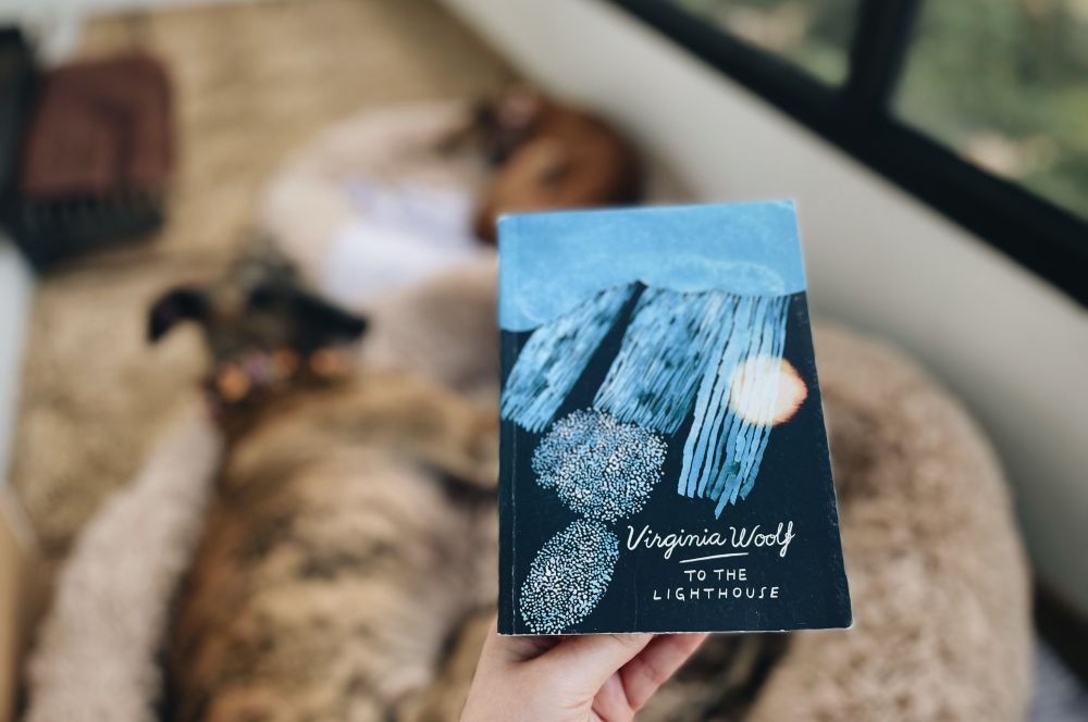 Kuvaajan kädessä Virginia Woolfin kirja To the Lighthouse. Taustalla kaksi koiraa. 