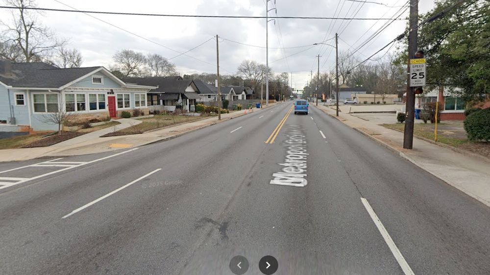 An urban 4-lane road fronted by houses. No way to cross the street despite a sad "School Zone" 25 MPH sign.