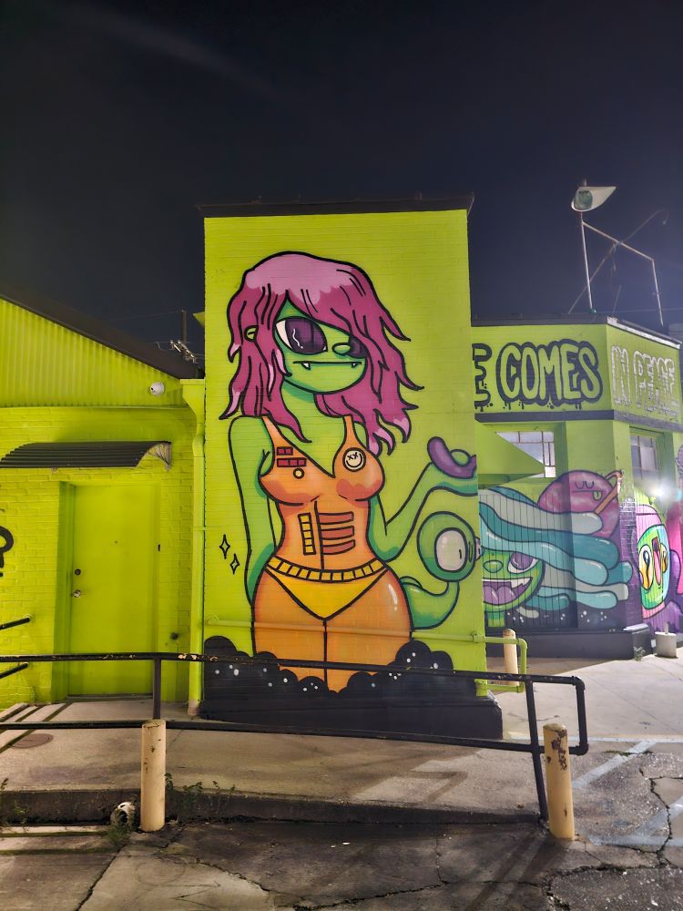a tall goblin looking alien woman mural on a green wall