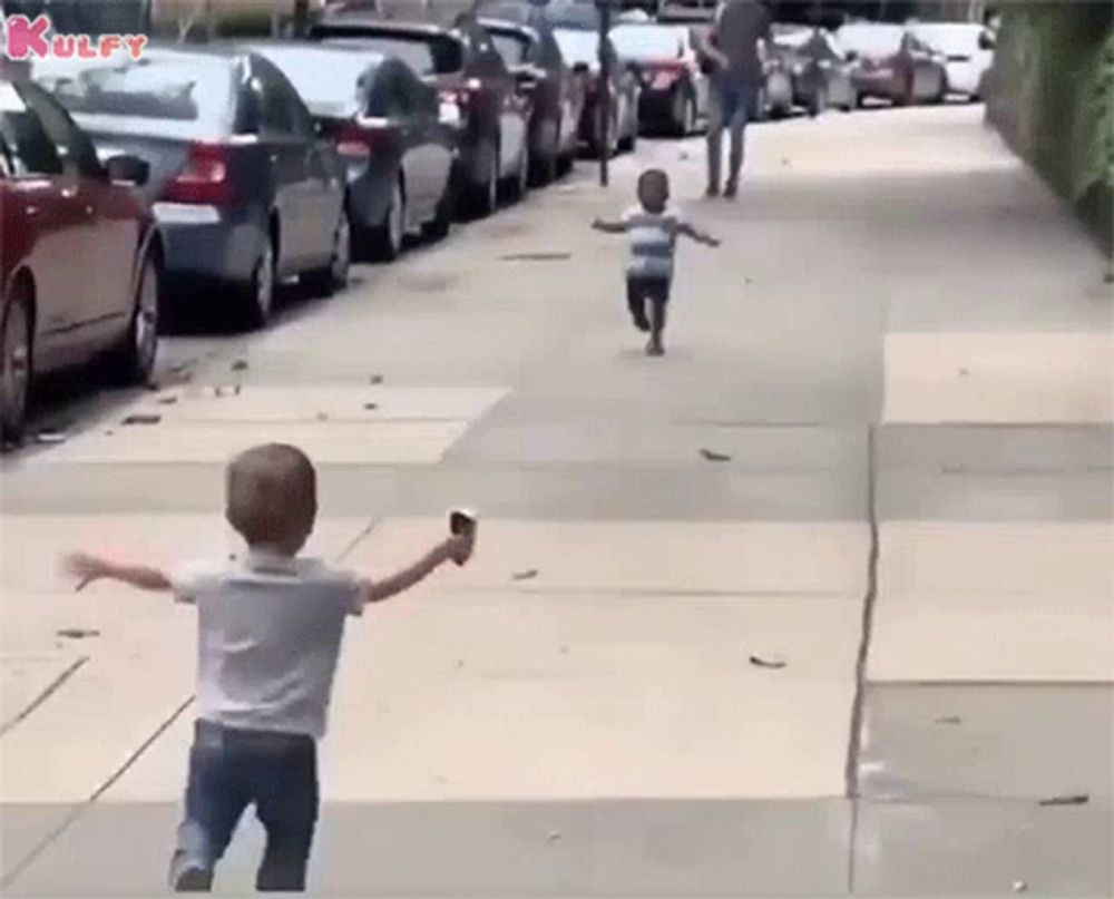 two young boys are running down a sidewalk and one is holding an ice cream cone