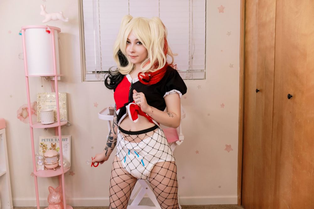 Medusa dressed as Harley Quinn, with fishnets covering her otherwise exposed white diaper. She's stood in the nursery in front of the high chair.