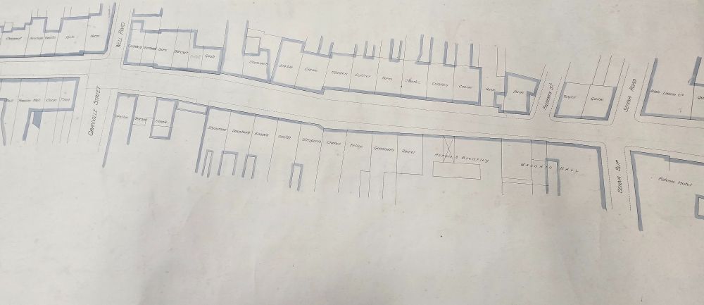 Colour photograph showing detail of plan in which the names of businesses and business owners can be seen. These are written in the spaces representing the properties ranged either side of Castle Street. Names include Curphey, Felice, Newson and Gore. Establishments include Heron & Brearley and the Falcon Hotel.