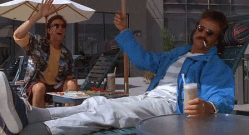 A clip from Weekend at Bernies: Bernie lies propped on a chaise lounge, a drink in his hand, sunglasses covering his eyes and a cigarette dangling from his lips. Larry (Andrew McCarthy) is cheerfully waving to someone offscreen as he pulls a cord, raising Bernies arm in an approximation of a wave.