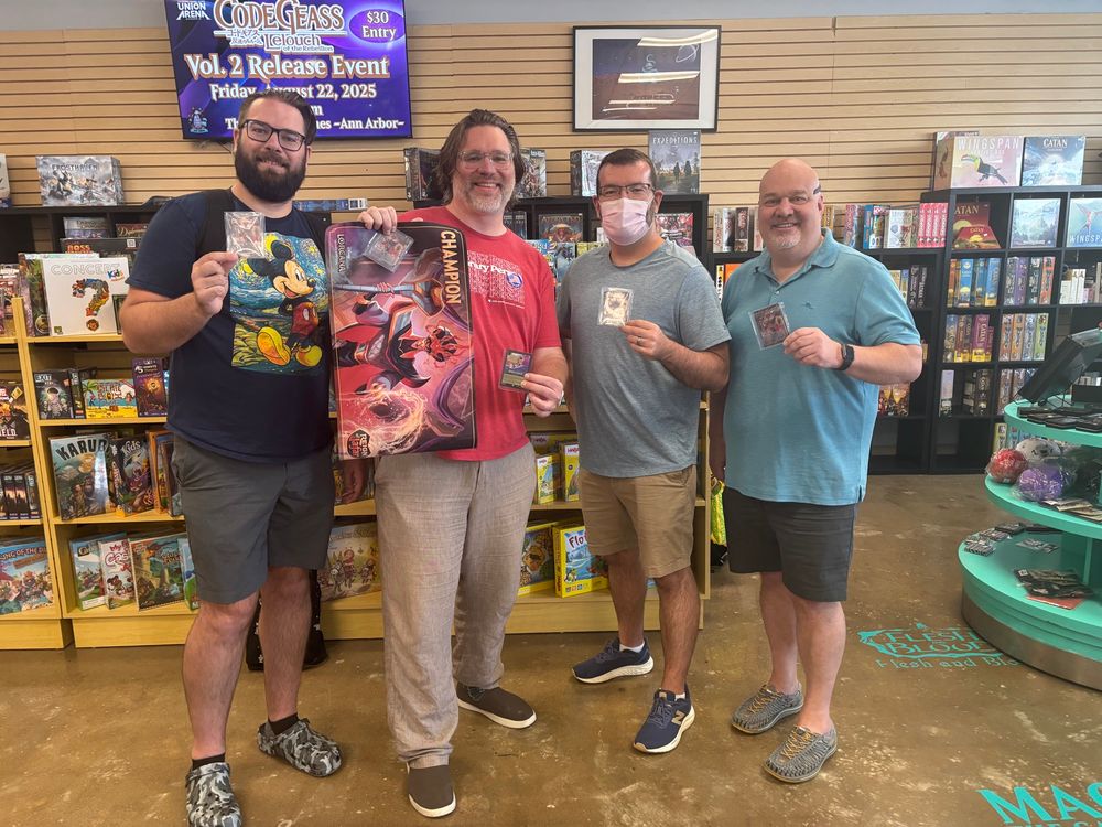 4 men standing in a gaming store holding prize cards and one holding a champion mat featuring Jafar from the movie Aladdin. 