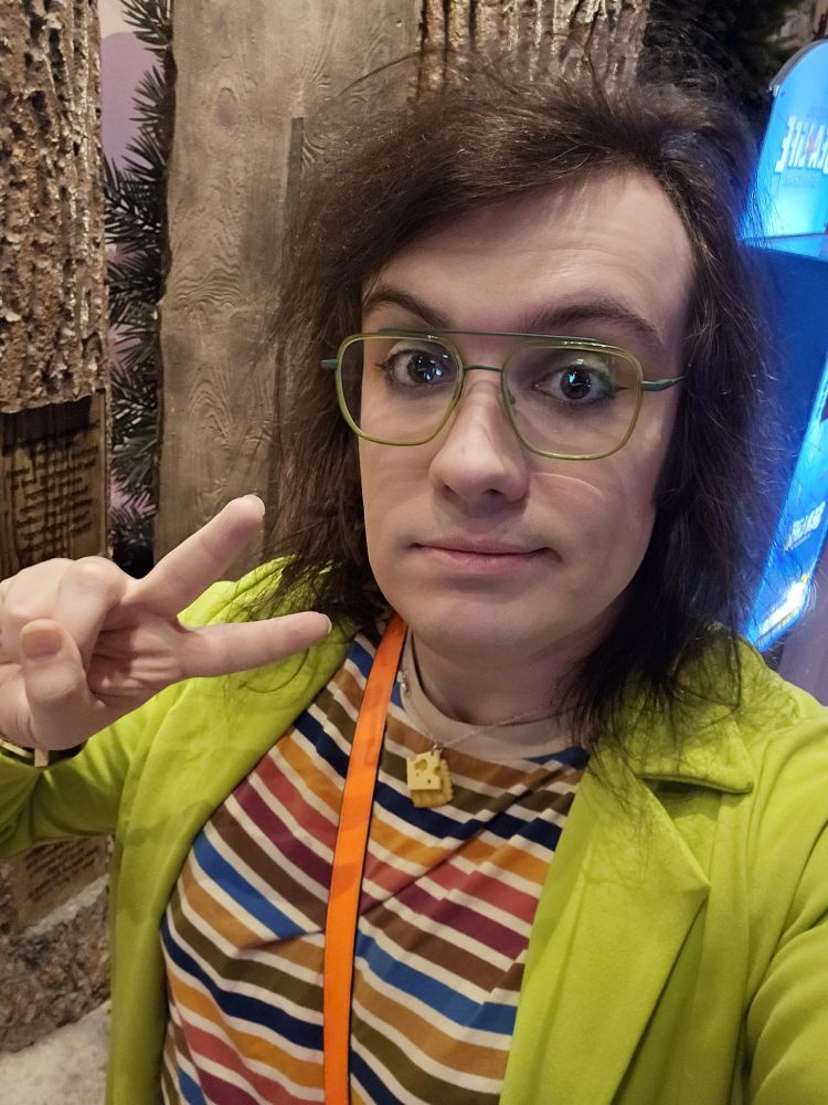 Stupes in a colourful striped shirt, lime green blazer, matching glasses, ever-exquisite eyeliner and a selection of cheese themed jewellery.