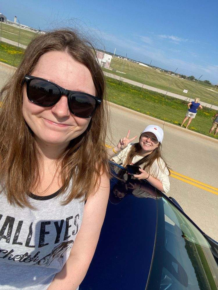 me sitting on the roof of my car and my sister behind me sitting on the window of the car at the airport observation lot