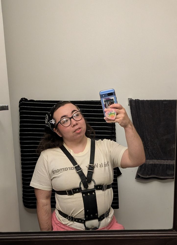 Bathroom mirror selfie, I am wearing a white shirt with black leather body harness overtop looking up at my camera