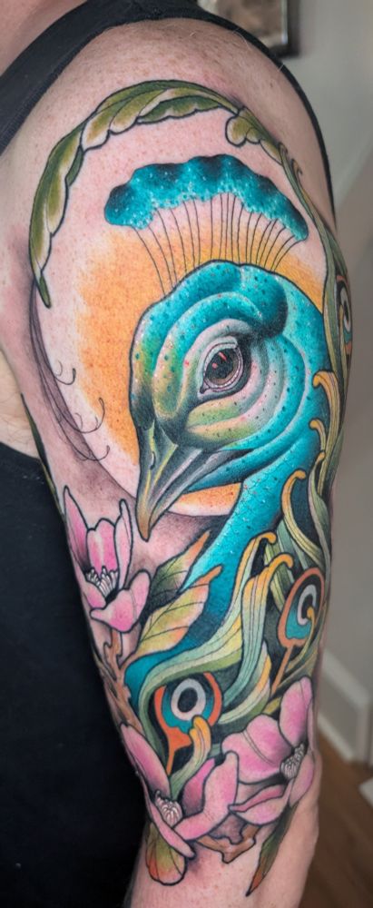 A colorful tattoo of a peacock head some tail feathers and flowers.