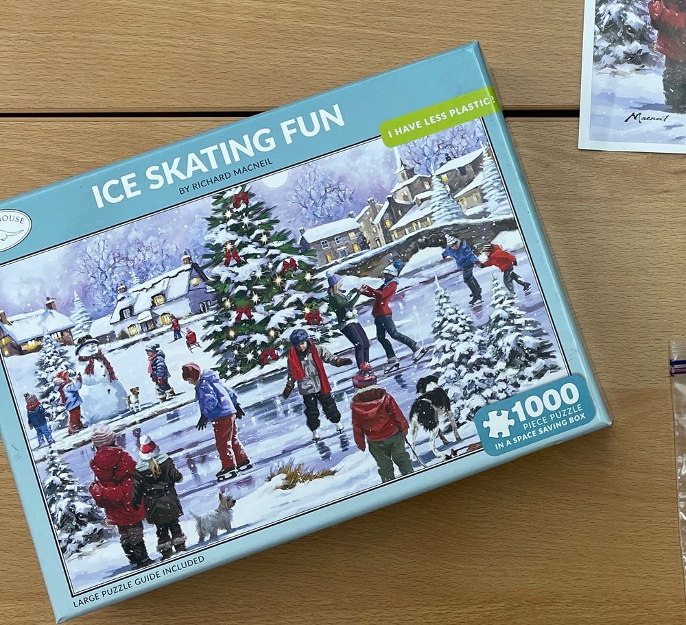 Cover of a puzzle box with an illustration of a snowy scene where people are iceskating around a Christmas tree.