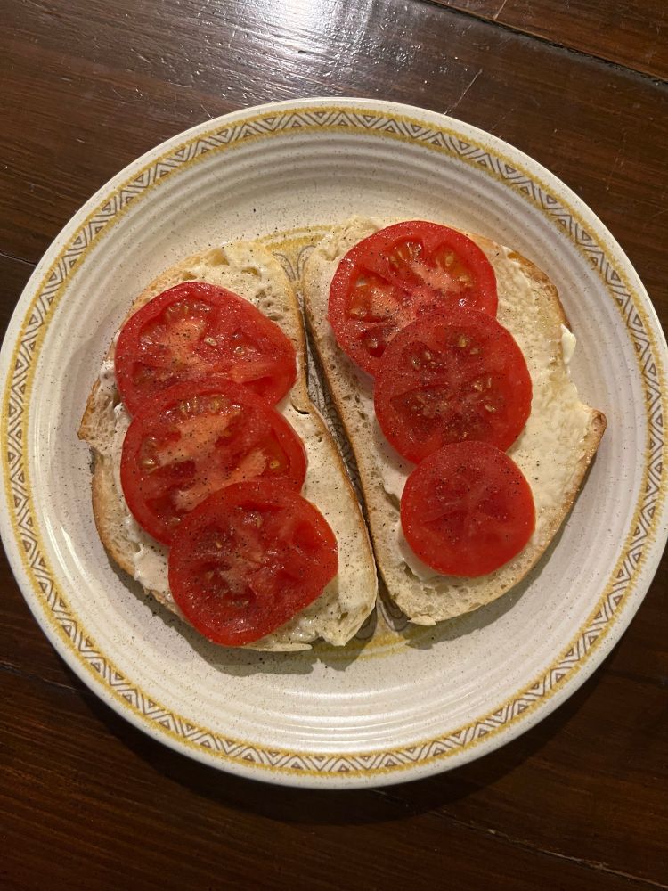 A juicy, red, garden-fresh tomato, sliced and arranged on a piece of mayo-slathered sourdough toast. 