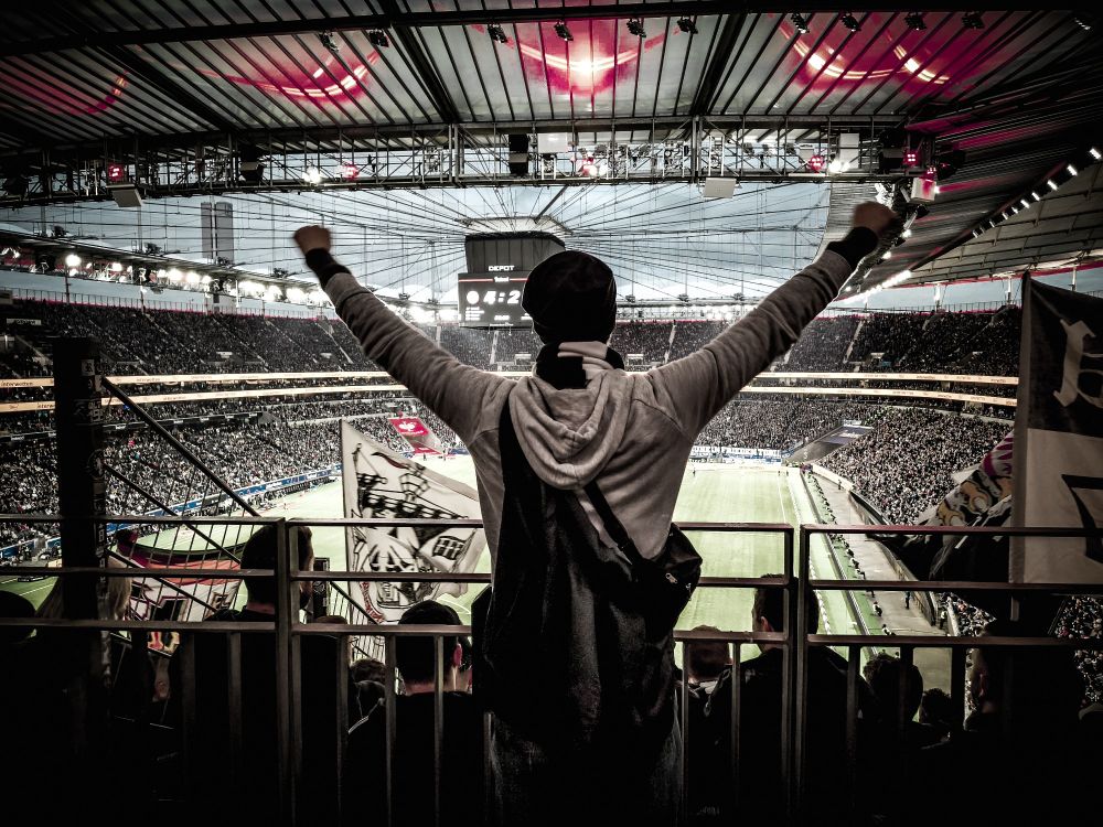 Das Bild zeigt mich in einem Fußballstadion (Waldstadion), der mit erhobenen Armen jubelt.  Der Spielstand auf der Anzeigetafel zeigt 4:2.