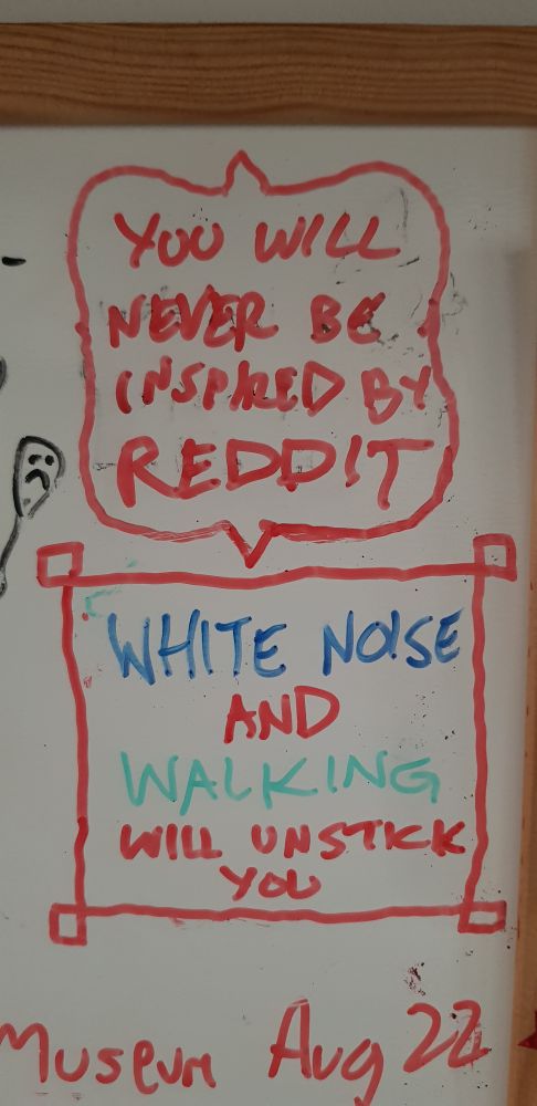 Two messages written on a whiteboard: 'you will never be inspired by Reddit' and 'white noise and walking will unstick you'