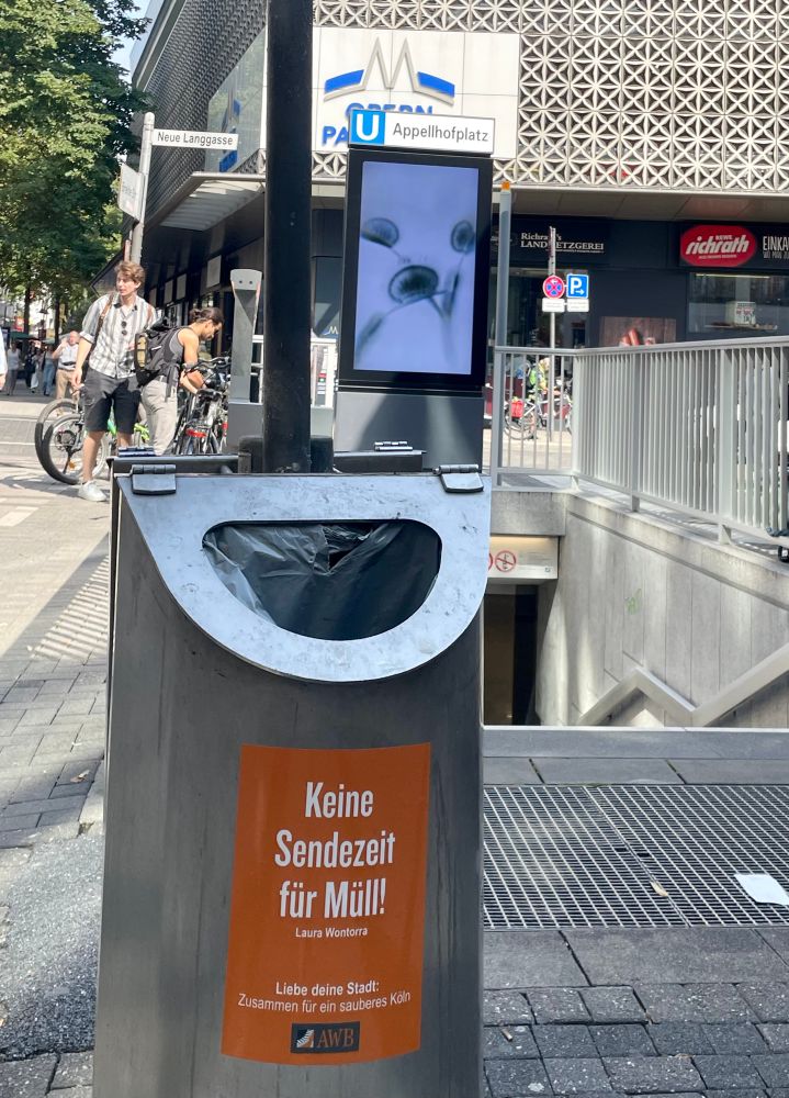 Oranger Aufkleber am Mülleimer am Apellhofplatz: „keine Sendezeit für Müll“. 